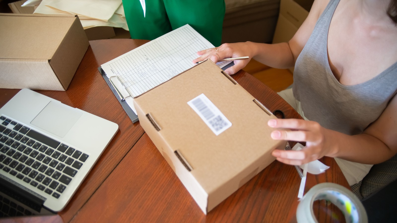 A packer sealing a labelled box at a desk beside a laptop and an order sheet