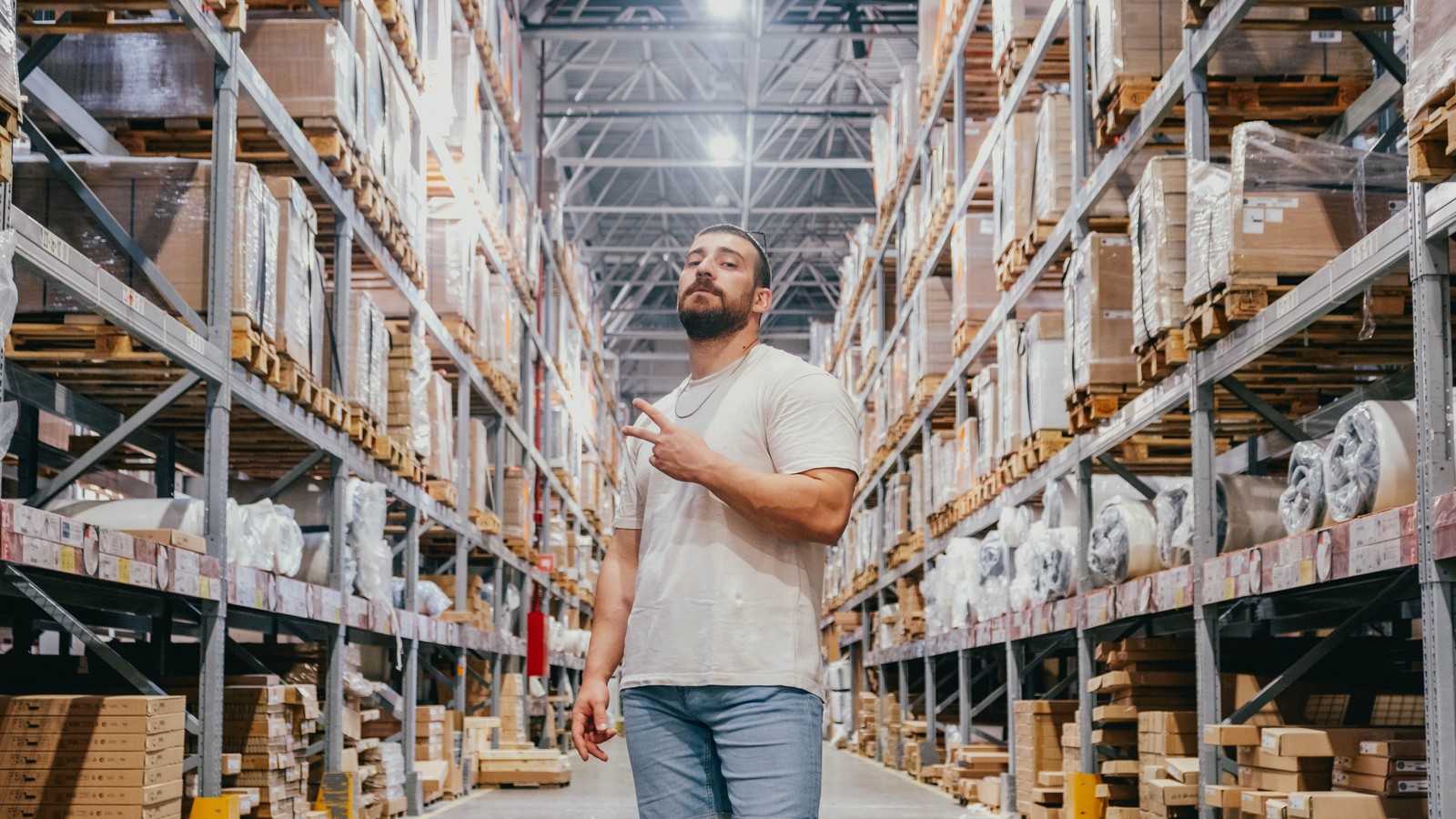 A buyer walking a wholesale warehouse aisle lined with stocked pallet racking