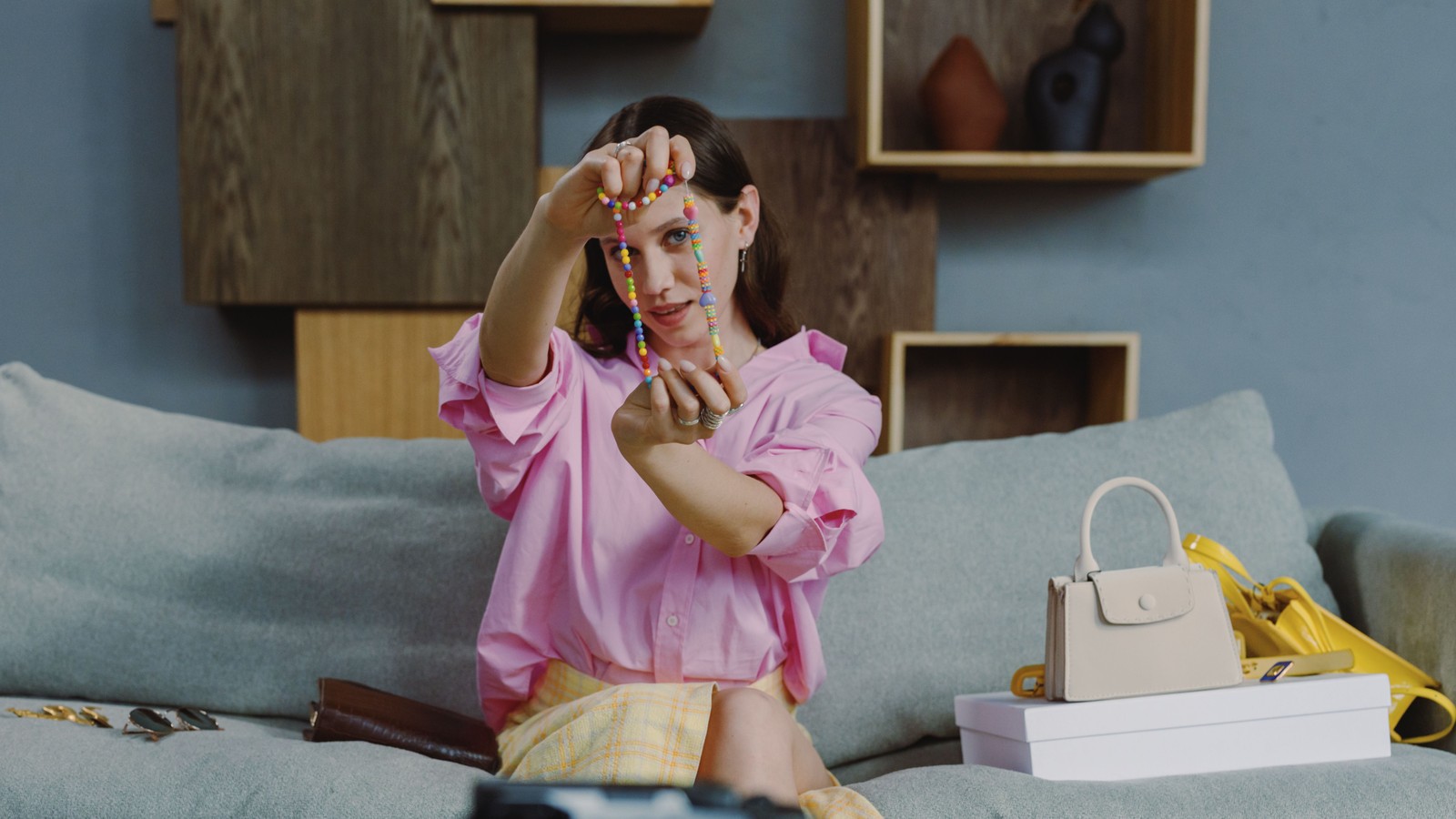 A live seller holding up a beaded necklace to the camera, with bags and boxes beside her