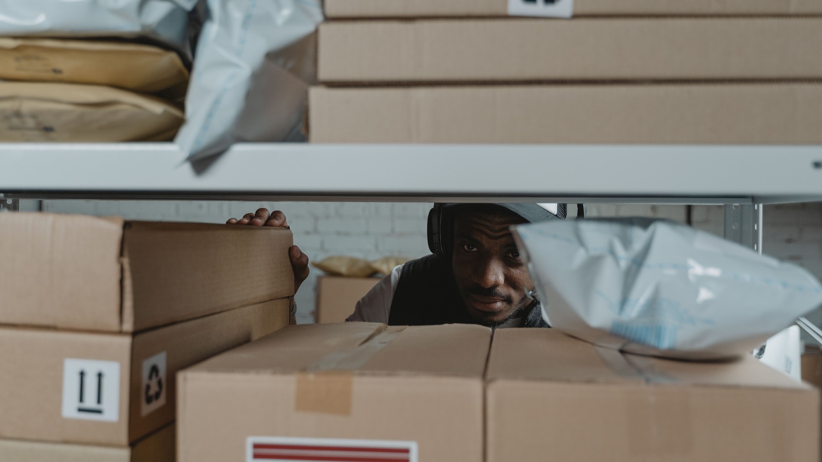 Warehouse worker peering between shelves of packed cartons and poly mailers