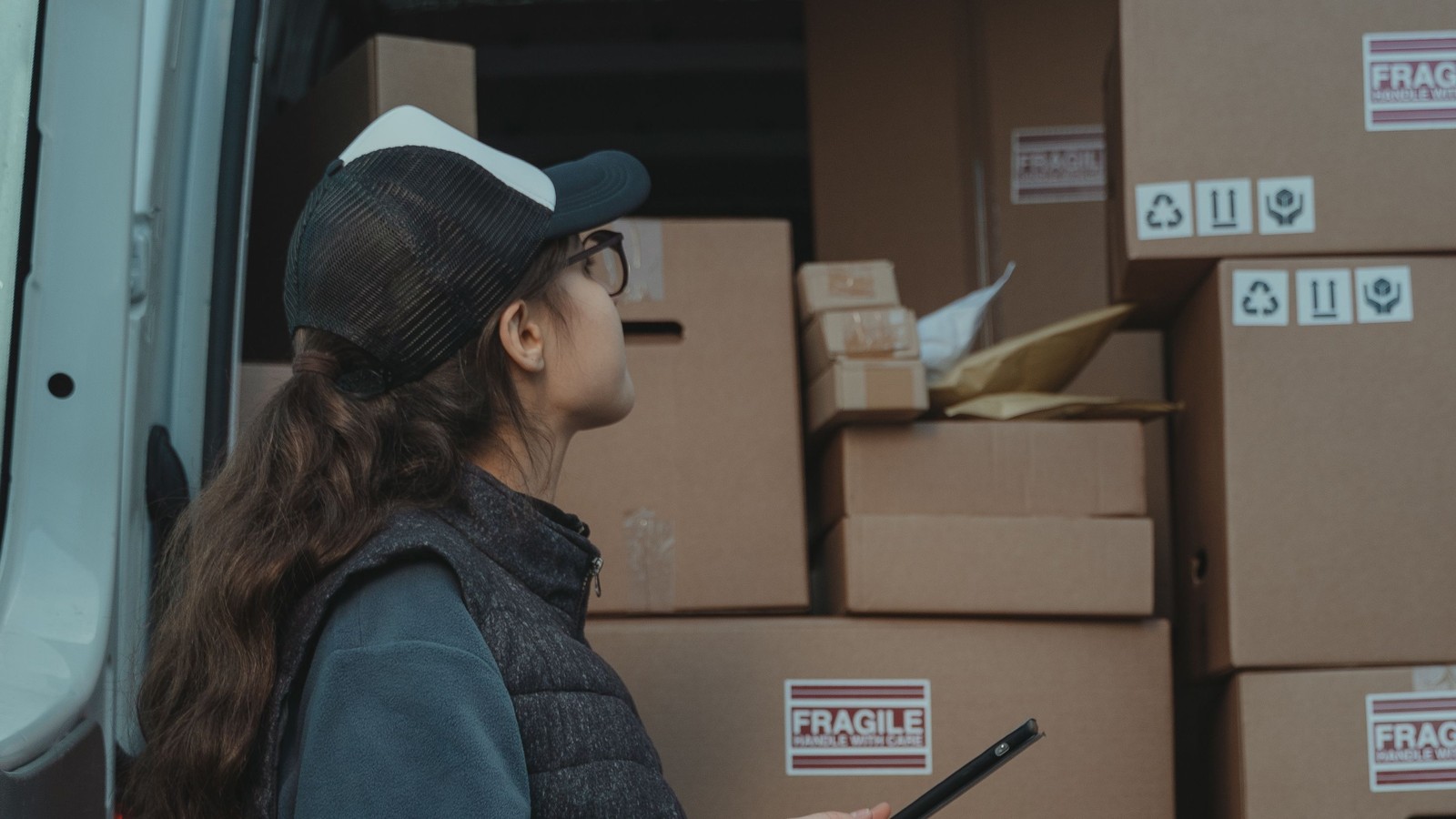 A worker with a scanner checking stacked fragile-labelled boxes in the back of a van