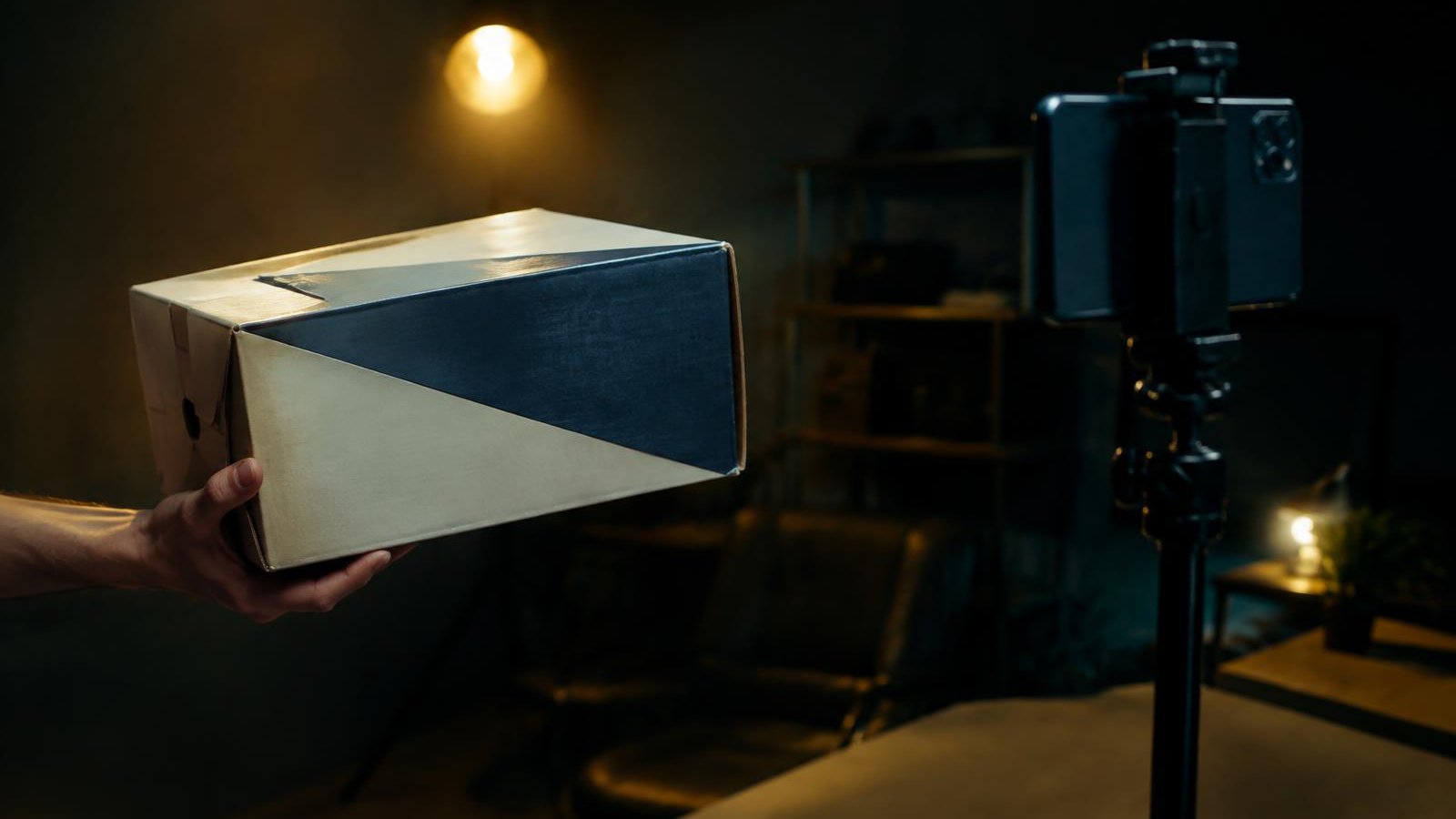 Hand holding a box up to a phone on a tripod in a dim studio